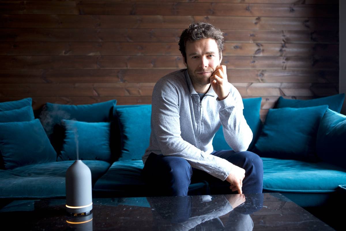 A man sitting on the couch with the aromatic scent coming from the black volant diffuser.
