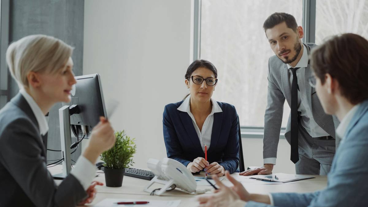 Businesswoman talking with male and female colleagues sitting at the table in modern office indoors